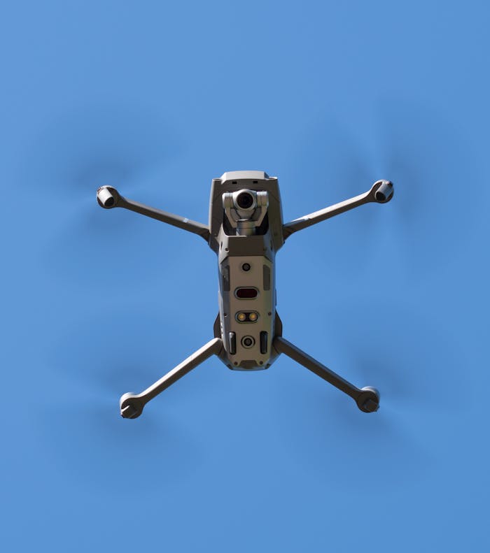 Aerial drone flying against a clear blue sky, captured from below.